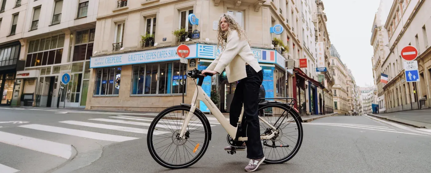 Une cycliste arrêtée sur un Heybike Helio U blanc crème à un passage piéton parisien